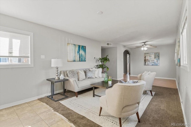 living area with arched walkways, ceiling fan, light tile patterned floors, visible vents, and baseboards