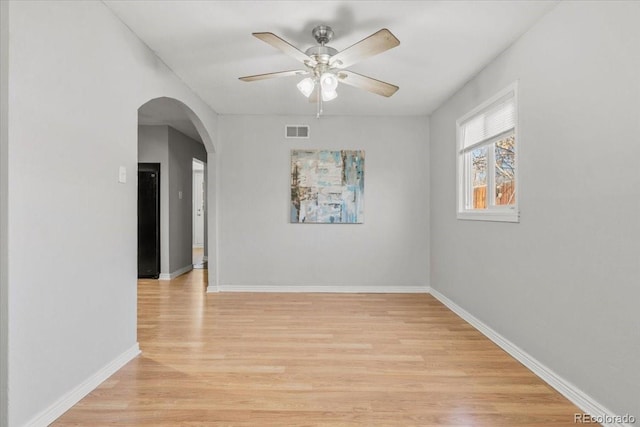 empty room featuring arched walkways, visible vents, light wood-style flooring, ceiling fan, and baseboards