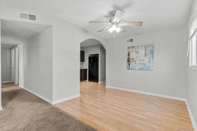 spare room featuring light wood-style floors, baseboards, visible vents, and arched walkways