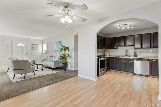 kitchen featuring light wood-style flooring, open floor plan, stainless steel appliances, light countertops, and a sink