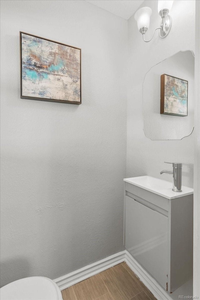 half bathroom featuring toilet, an inviting chandelier, vanity, and baseboards