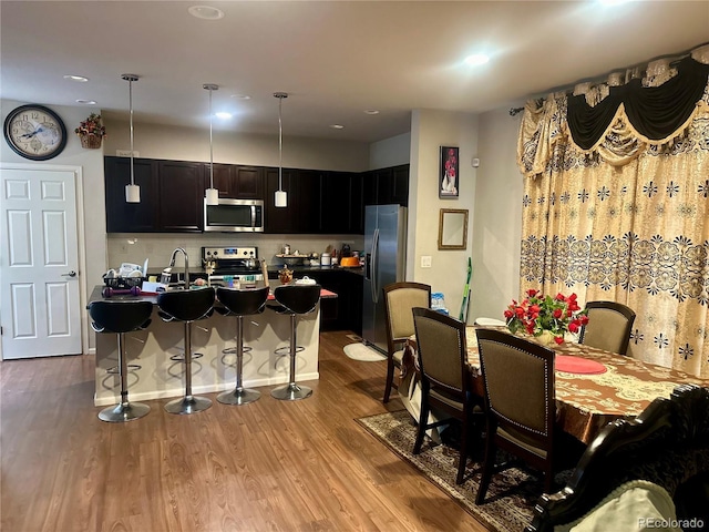 15600 Bolling, Denver, CO 80239 - kitchen featuring appliances with stainless steel finishes, a kitchen breakfast bar, wood finished floors, recessed lighting, and dark cabinetry