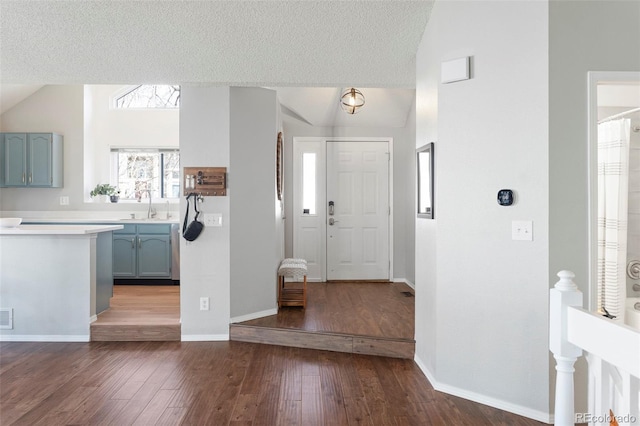 entrance foyer with dark wood-style floors, vaulted ceiling, a textured ceiling, and baseboards