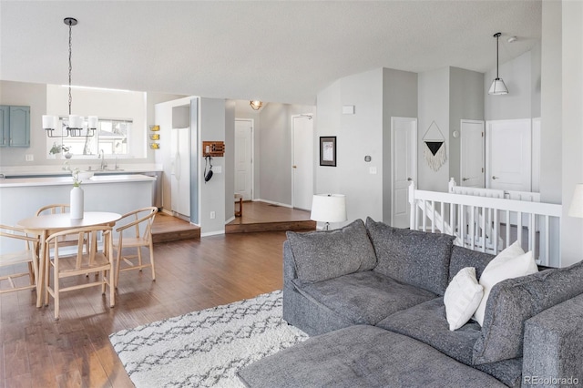 living room featuring dark wood finished floors, lofted ceiling, an inviting chandelier, a textured ceiling, and baseboards