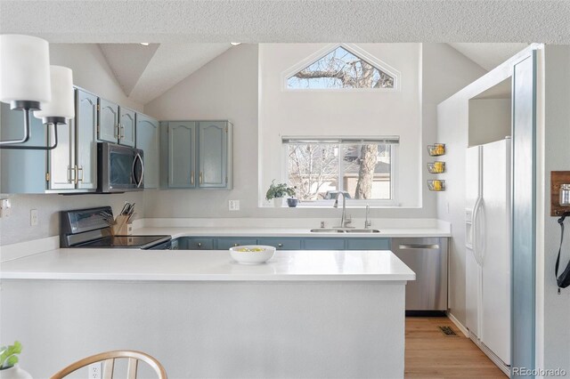 kitchen with lofted ceiling, a peninsula, a sink, light countertops, and appliances with stainless steel finishes