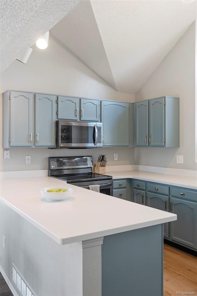 kitchen featuring appliances with stainless steel finishes, light wood-type flooring, vaulted ceiling, and a peninsula