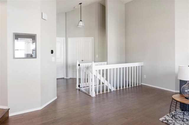 hall with baseboards, high vaulted ceiling, wood finished floors, and an upstairs landing