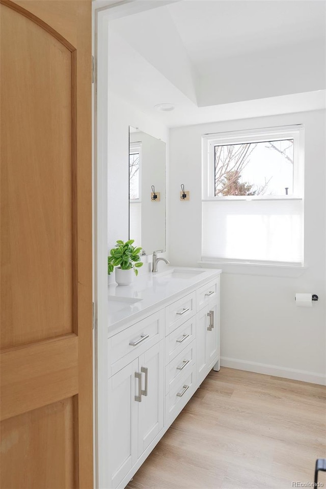 full bathroom with double vanity, a sink, baseboards, and wood finished floors