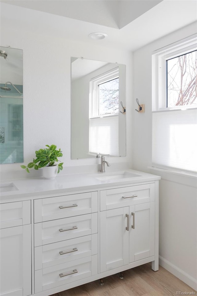 bathroom featuring double vanity, wood finished floors, a shower, and a sink