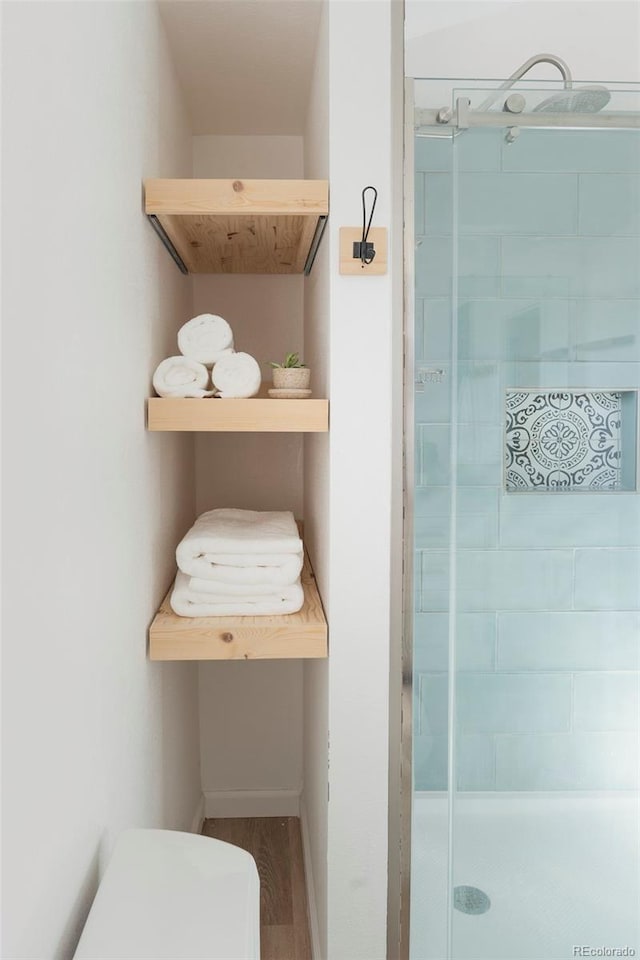 bathroom featuring toilet, a shower stall, baseboards, and wood finished floors