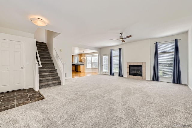unfurnished living room featuring carpet floors, stairway, ceiling fan, a fireplace, and baseboards