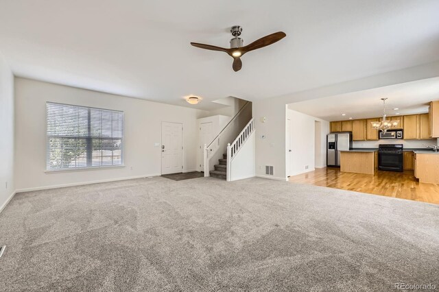 unfurnished living room with light carpet, a chandelier, baseboards, ceiling fan, and stairs