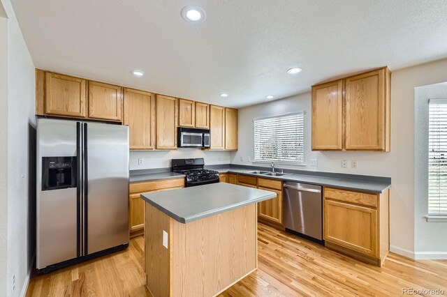 kitchen with stainless steel appliances, a sink, light wood-style floors, a kitchen island, and recessed lighting