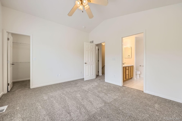 unfurnished bedroom featuring light colored carpet, vaulted ceiling, a spacious closet, ensuite bathroom, and baseboards