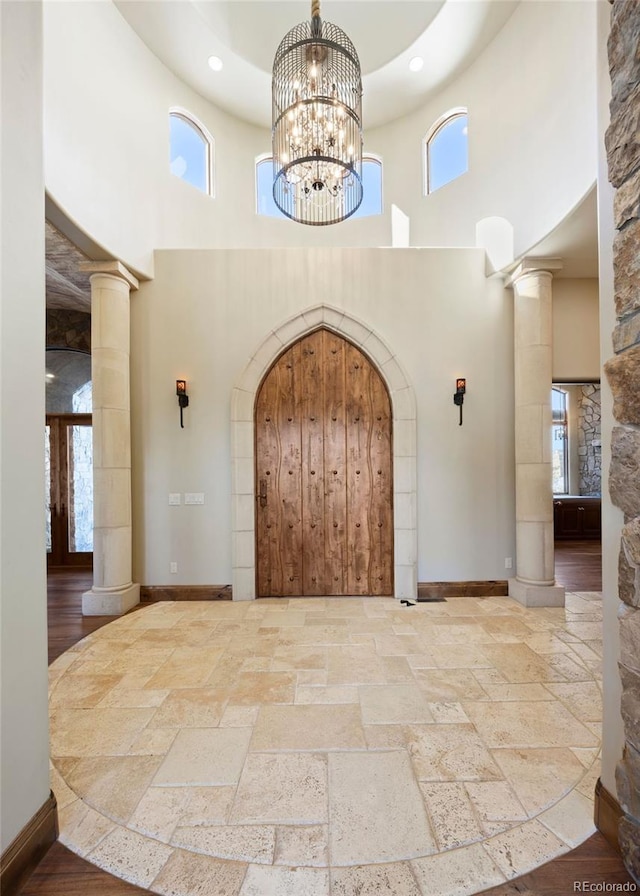 interior space with ornate columns, a high ceiling, baseboards, and stone tile flooring