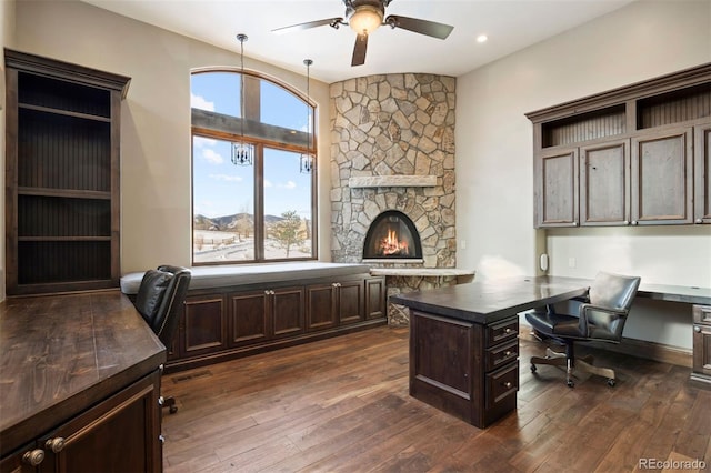 home office with visible vents, a ceiling fan, dark wood-type flooring, a fireplace, and built in desk