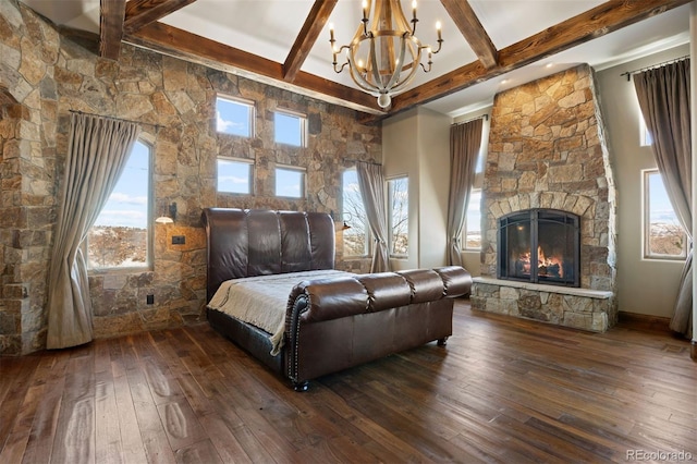 bedroom featuring a stone fireplace, beam ceiling, and multiple windows