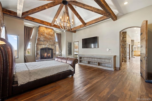 bedroom featuring dark wood-type flooring, beamed ceiling, a stone fireplace, and an inviting chandelier