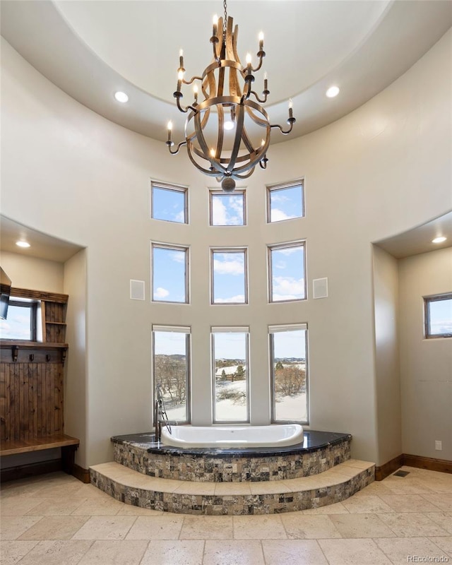 foyer featuring baseboards, a towering ceiling, stone tile flooring, a notable chandelier, and recessed lighting