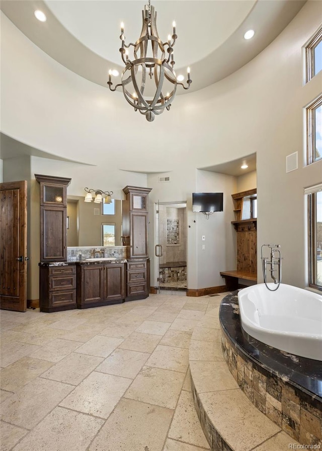 bathroom featuring plus walk in shower, a high ceiling, a notable chandelier, and vanity