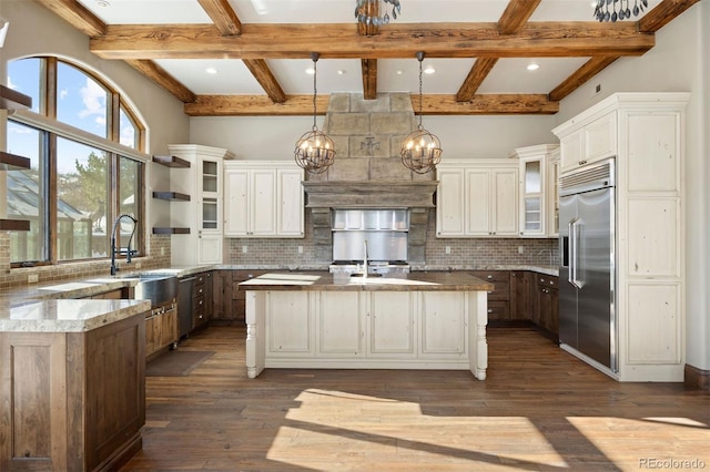 kitchen with built in refrigerator, a large island, light stone countertops, glass insert cabinets, and pendant lighting