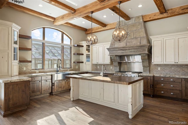 kitchen with hanging light fixtures, open shelves, an island with sink, dark stone countertops, and glass insert cabinets