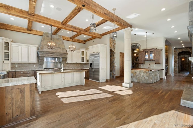 kitchen with built in refrigerator, hanging light fixtures, decorative columns, and a spacious island