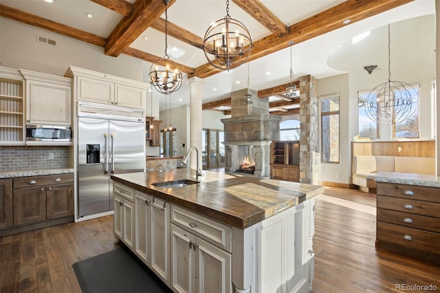 kitchen featuring pendant lighting, a large fireplace, a kitchen island with sink, a sink, and built in appliances