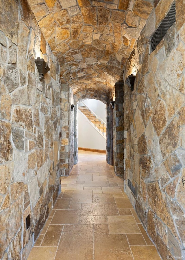 corridor featuring brick ceiling, stone tile floors, stairs, and arched walkways