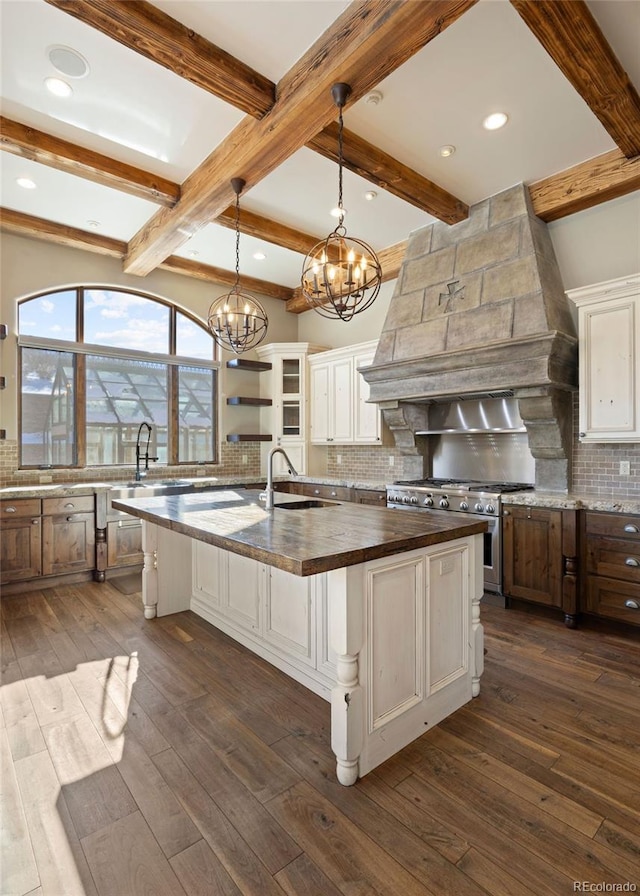 kitchen featuring a center island with sink, custom range hood, glass insert cabinets, decorative light fixtures, and a sink