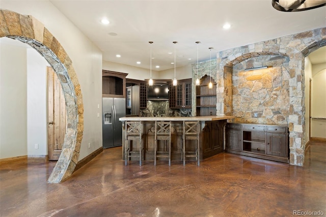 interior space with stainless steel refrigerator with ice dispenser, pendant lighting, dark brown cabinetry, and a kitchen bar