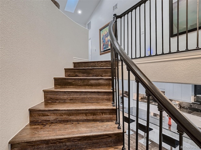 staircase featuring visible vents, a textured wall, and vaulted ceiling