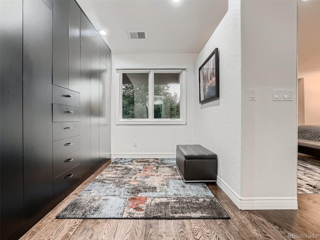 hall featuring baseboards, wood finished floors, and visible vents