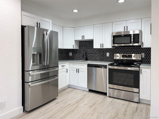 kitchen with white cabinetry, backsplash, stainless steel appliances, and light hardwood / wood-style floors