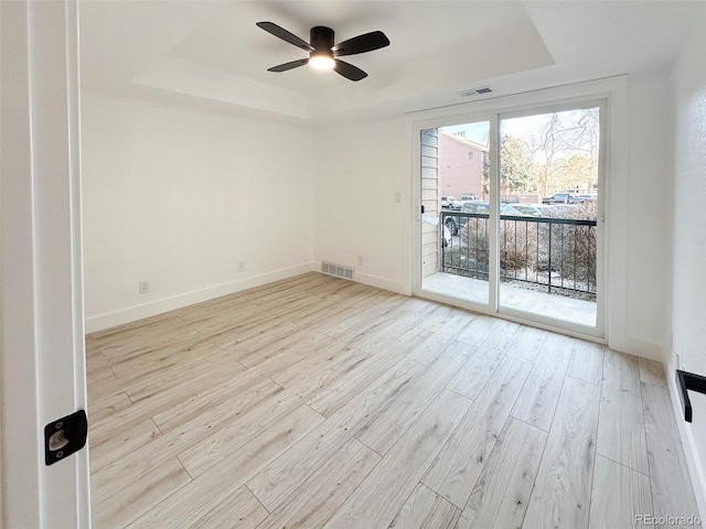 unfurnished room with light hardwood / wood-style flooring, ceiling fan, and a tray ceiling