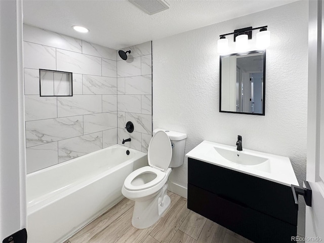 full bathroom featuring tiled shower / bath, hardwood / wood-style flooring, vanity, toilet, and a textured ceiling