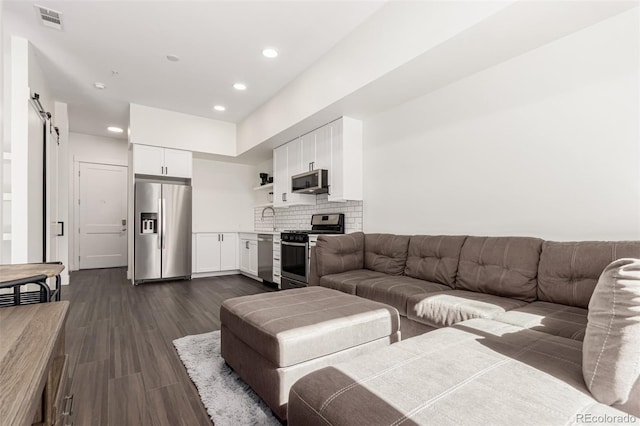 living area featuring dark wood-style floors, recessed lighting, visible vents, and a barn door