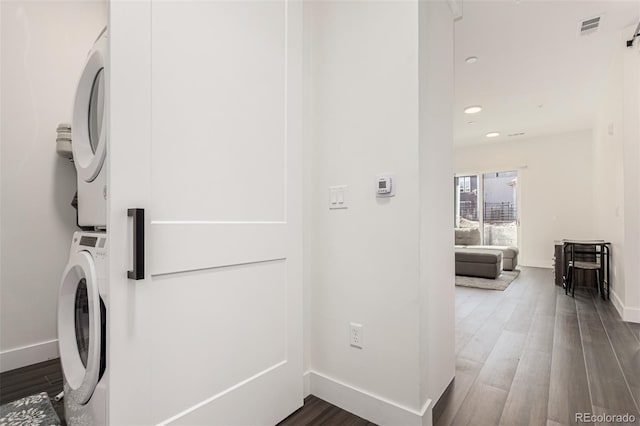 clothes washing area with laundry area, stacked washer / dryer, wood finished floors, and baseboards