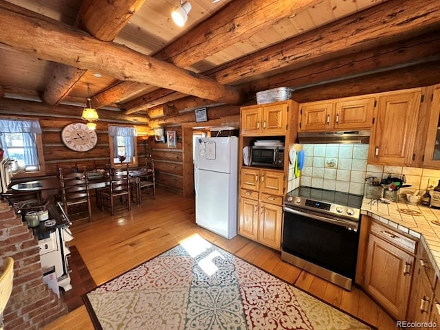 kitchen featuring rustic walls, white refrigerator, tile counters, stainless steel electric stove, and decorative backsplash