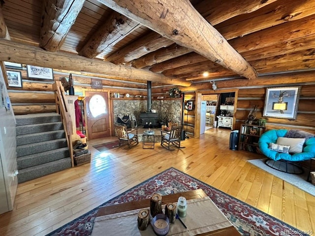 unfurnished living room with beam ceiling, hardwood / wood-style floors, log walls, and a wood stove