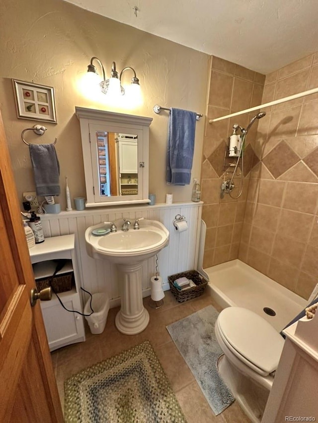 bathroom with toilet, tile patterned flooring, and a tile shower