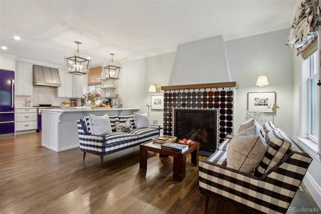 living room featuring crown molding, dark wood-style flooring, a brick fireplace, and a chandelier