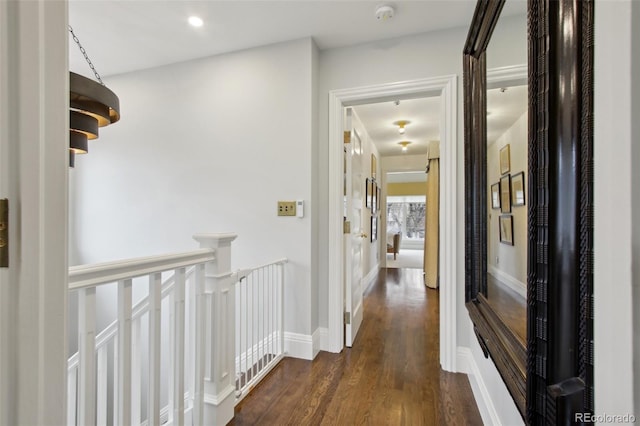 corridor with dark wood-style flooring, an upstairs landing, and baseboards