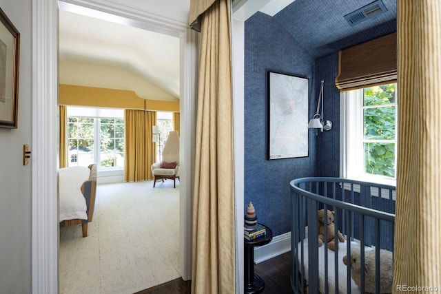bedroom with wood finished floors, visible vents, a crib, and vaulted ceiling