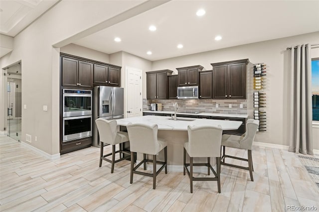 23696 E Del Norte Pl, Aurora, CO 80016 - kitchen with appliances with stainless steel finishes, a breakfast bar area, backsplash, a kitchen island with sink, and dark brown cabinets