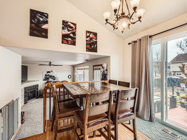 dining room with lofted ceiling, ceiling fan with notable chandelier, wood finished floors, visible vents, and a tile fireplace