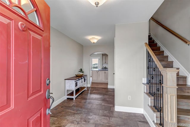 foyer with arched walkways, stairway, and baseboards