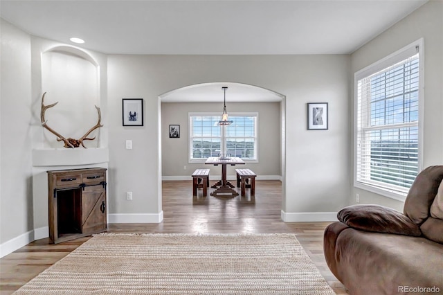 living room featuring arched walkways, light wood-type flooring, baseboards, and a chandelier