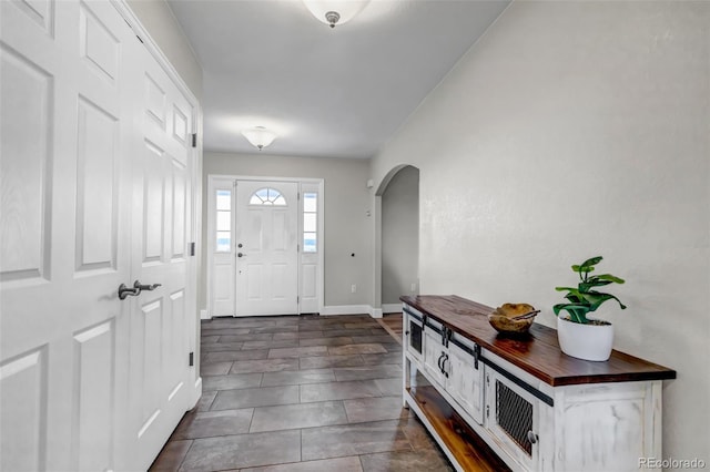 foyer entrance with arched walkways, baseboards, and dark tile patterned flooring
