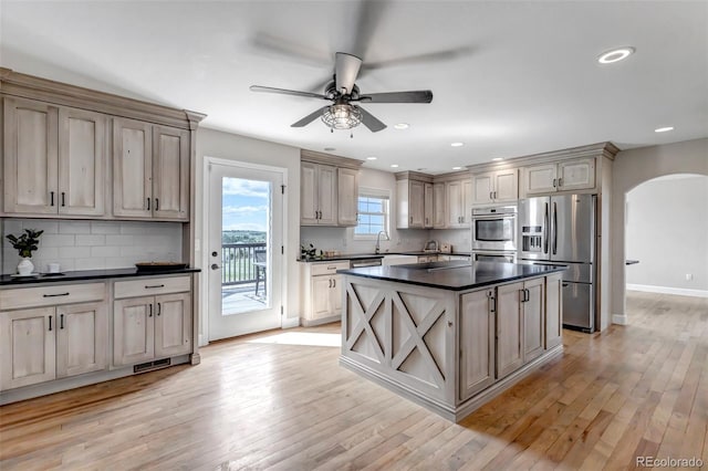 kitchen with appliances with stainless steel finishes, arched walkways, dark countertops, a ceiling fan, and backsplash